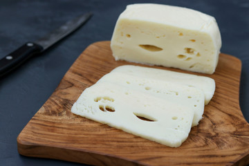 Suluguni Georgian cheese sliced on a wooden board against a dark background