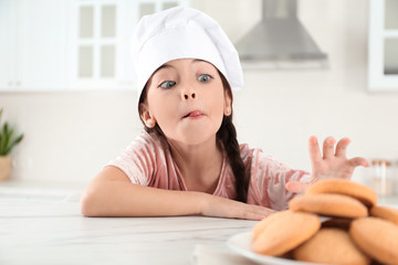 Cute little girl wearing chef hat at table in kitchen