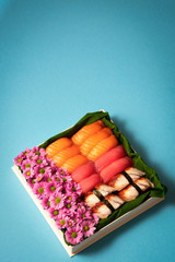 Sushi set with flowers in gift box on bright blue background. Like creative chocolate candy box.Valentines Day (14 February), Mother's day, Birthday, Woman's day (8 March) or spring concept.Copy space