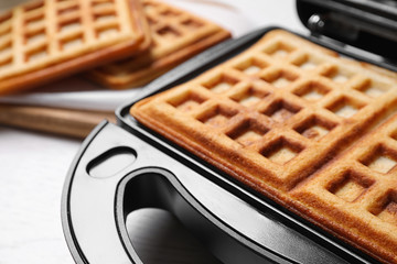 Modern iron with tasty Belgian waffles on table, closeup
