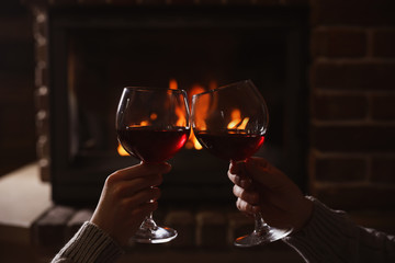 Couple with glasses of red wine near burning fireplace, closeup