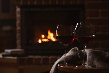 Glasses of red wine on wooden table near fireplace. Space for text
