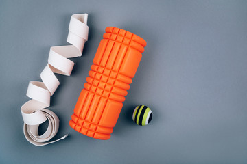 Set of green myofascial release and massage ball, orange bumpy foam massage roller for trigger points and white belt over grey background. Self body care massage and stress, pain relief. Sport concept