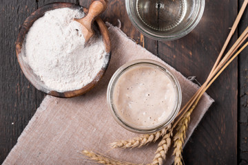 Fresh homemade bubbly sourdough starter, a fermented mixture of water and flour to use as leaven for bread baking, on wooden table