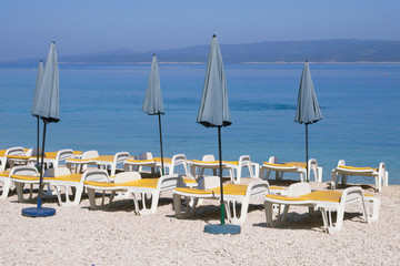Fototapeta na wymiar Blue umbrellas and loungers for relax and comfort on sea beach. Happy summer vacations and tourism concept. Paid service on beaches.