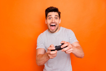 Photo of funny attractive cheerful guy hold hands joystick playing video games excited gamer riding speed car to finish wear striped t-shirt isolated bright orange color background