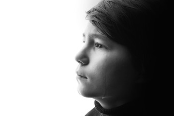 Black and white portrait of young sad boy crying with sad eyes. White background. Free space for text. Tear on cheek of unhappy teenager.