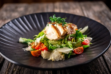 Caesar salad with fresh vegetables and crispy chicken on wooden background