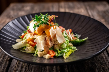 Caesar salad with fresh vegetables and crispy chicken on wooden background