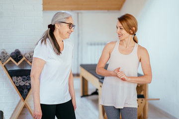 Obraz premium Positive friendly smiling female pilates instructor meeting mature elderly woman in pilates studio.