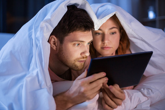 technology, internet and people concept - couple using tablet pc computer in bed at night