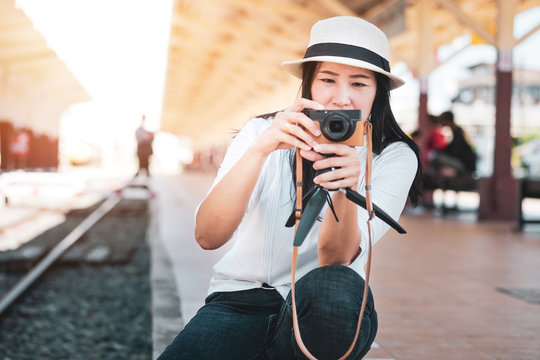 Asian woman tourist wearing a white T-shirt, wearing a hat, holding a camera and taking pictures at the train station