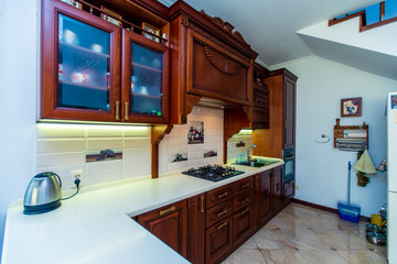 Antique wooden kitchen set made of mahogany. The furniture is covered with wood carvings. Gas stove, extractor hood, dishes