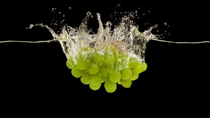 Juicy green grapes splashing into fresh water on black background, panorama
