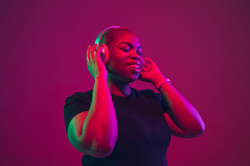 Listen to music. African-american young woman's portrait on purple background. Beautiful model in wireless headphones. Concept of emotions, facial expression, sales, ad, inclusion. Copyspace.