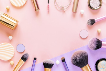 Makeup brushes, sponges and decorative cosmetics on purple and pink colored background. Top view, copy space