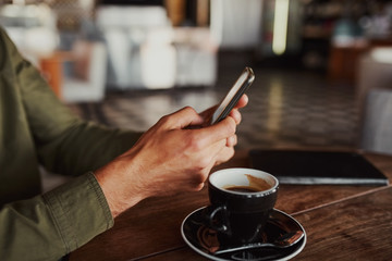 Closeup of man hands using smartphone while sitting in cafe drinking coffee