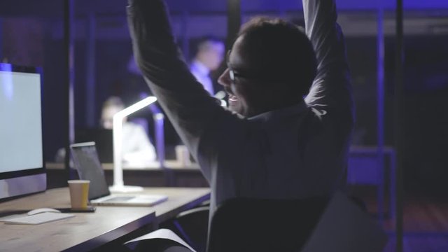 Happy man rejoicing sitting in office late at night.