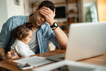 Young father feeling stressed while babysitting and working at home.
