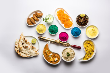 Happy Holy concept  showing Indian assorted lunch food like paneer butter masala, naan, jeera rice, black chana fry, jalebi, fujiyama, thandai and Farsan with holi colours and pichkari 