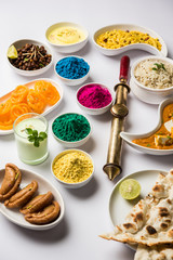 Happy Holy concept  showing Indian assorted lunch food like paneer butter masala, naan, jeera rice, black chana fry, jalebi, fujiyama, thandai and Farsan with holi colours and pichkari 