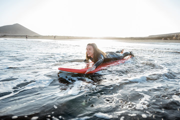 Young woman in wetsuit catching water flow on the surfboard, surfing on the wavy ocean during a sunset. Water sports and active lifestyle concept