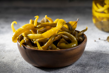 pickled spicy green pepper pods in an wooden bowl on a gray background and a wooden bowl with pepper pods, closeup