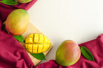 flat lay ripe juicy whole and slice of exotic mango with leaves on wooden plate on white and red background. copy space, soft focus, banner, text, blank