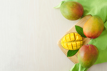 flat lay ripe juicy whole and slice of exotic mango with leaves on wooden plate on white and green background. copy space, soft focus