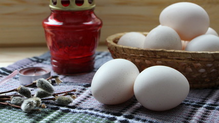 poultry eggs on a table and in a basket next to a red lamp and a pussy-willow branch with fluffy buds