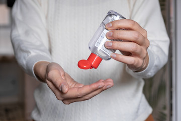 Close up of a girl with a white jumper cleaning her hands with some antibacterial sanitizer, blurred background