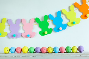 Colorful Easter eggs and handmade bunny easter garland on beige background.