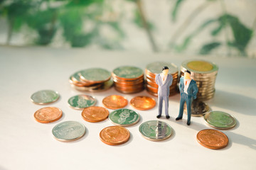 Miniature people, couple businessman standing with stack coins using as business and financial concept