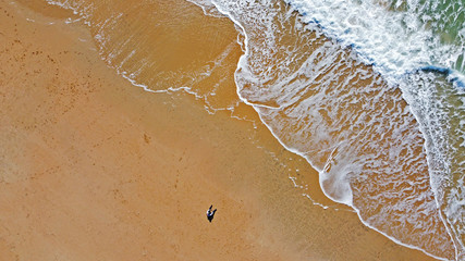 Fototapeta na wymiar Imagen cenital de la playa de Camposoto en San Fernando en la provincia de Cádiz. Un hombre sentado sobre la arena cerca del agua y las olas