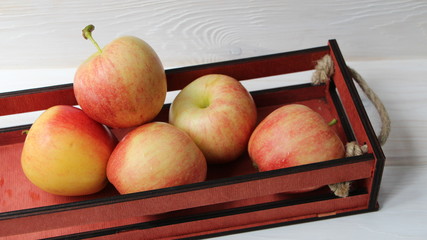 slide of reddish apples in a decorative wooden crate against a textured white wood