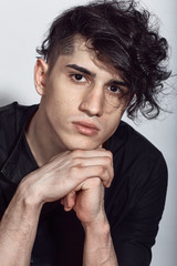 Young guy in a black shirt similar to Adriano Celentano posing on a white background. Fashion portrait