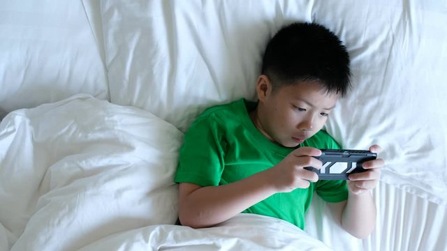 asian chinese boy playing smartphone on bed, kid use phone and play game, addicted game and cartoon, 