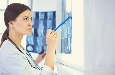 Young smiling female doctor with stethoscope pointing at X-ray at doctor's office