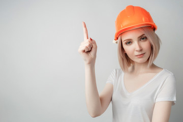 Portrait of a young girl in a white T-shirt and a construction helmet on a white background, showing thumbs up