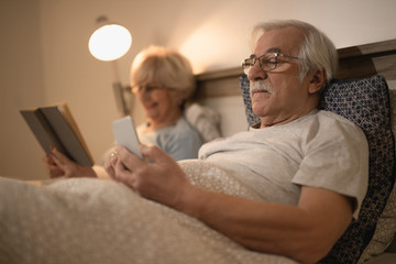 Fototapeta premium Senior man using cell phone in bed at night.