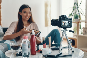 Happy young woman applying make-up palette and smiling while making social media video