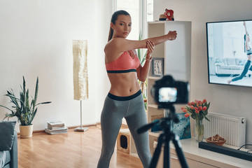 Fototapeta na wymiar Attractive young woman in sports clothing working out and smiling while making social media video