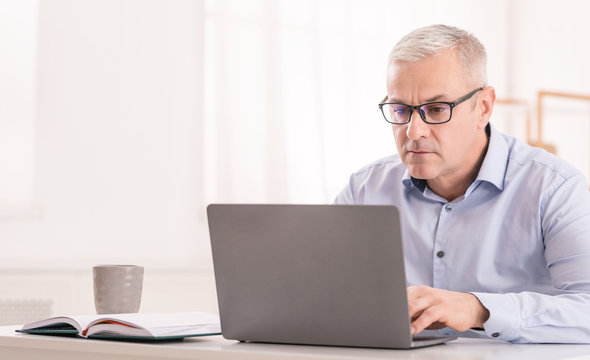 Serious senior man using laptop at office