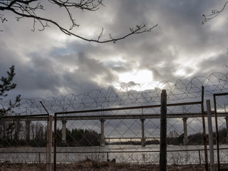 Fence with barbed wire rings on the river Bank near the bridge on a spring day