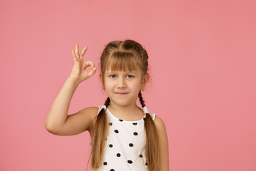 Cute smiling little child girl making Ok gesture on pink background.