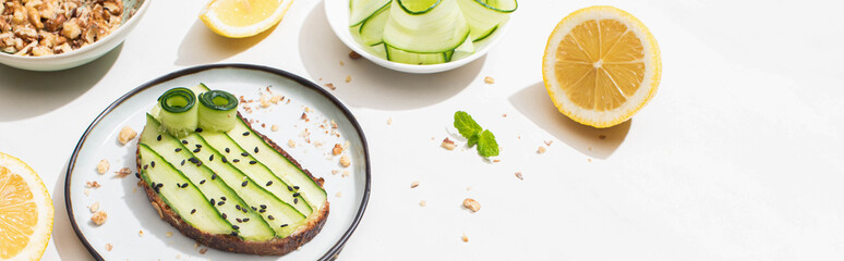 fresh cucumber toast with seeds near mint leaves and lemon on white background, panoramic shot