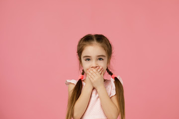 beautiful little girl in dress asking to be quiet. child closes her mouth with her hand. I will not tell anyone