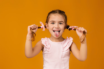 happy funny little child girl showing her tongue on yellow background. facial expression
