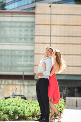 Portrait of a young romantic couple. Woman in red dress hugs her husband on the background on blurred building in Warsaw, Poland