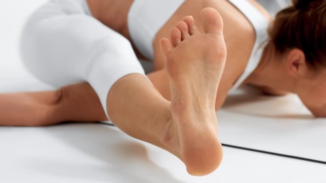 Senior woman in white space practice yoga closeup of toe in a stretching position is lifted up